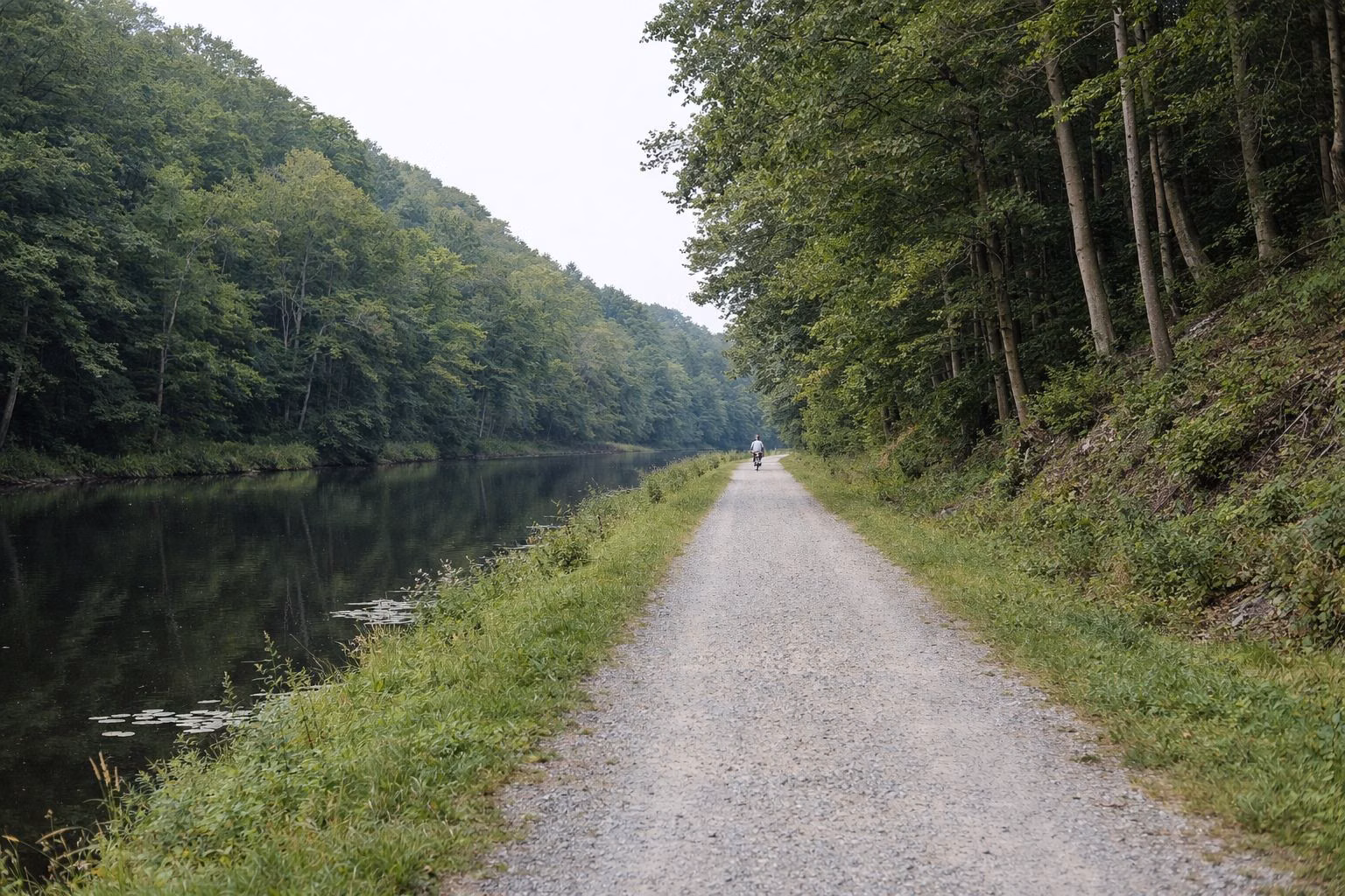 A flat gravel towpath beside a narrow tree-lined canal