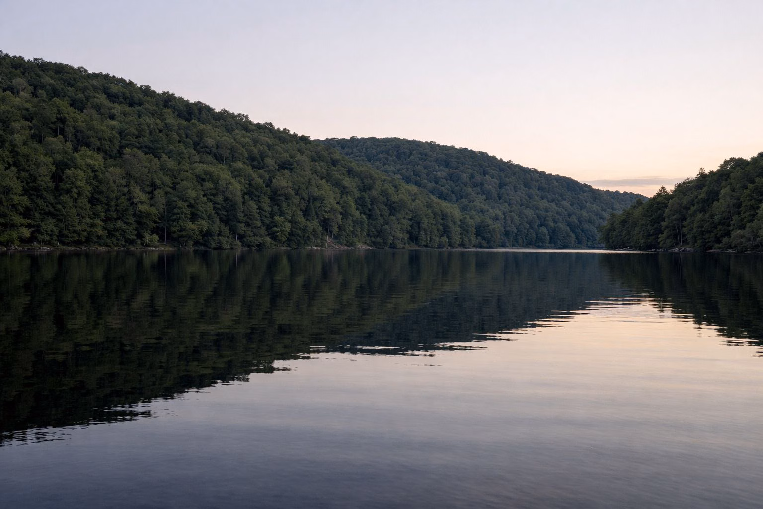 Calm lake water at dusk reflecting forested hills